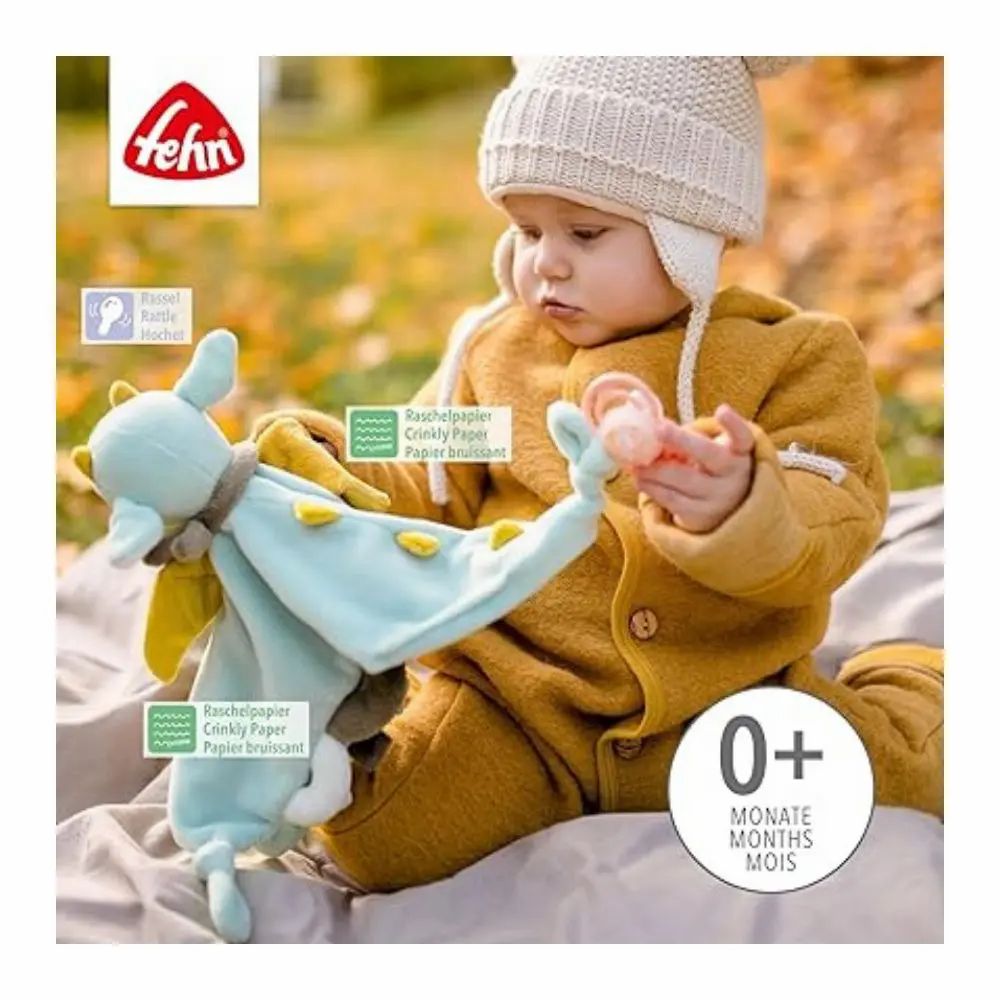 Baby hält Stoffdrachen. Marke: Fehn. Text: "0+ MONATE MOIS MONTHS". Auf dem Drachen: Raschelpapier.