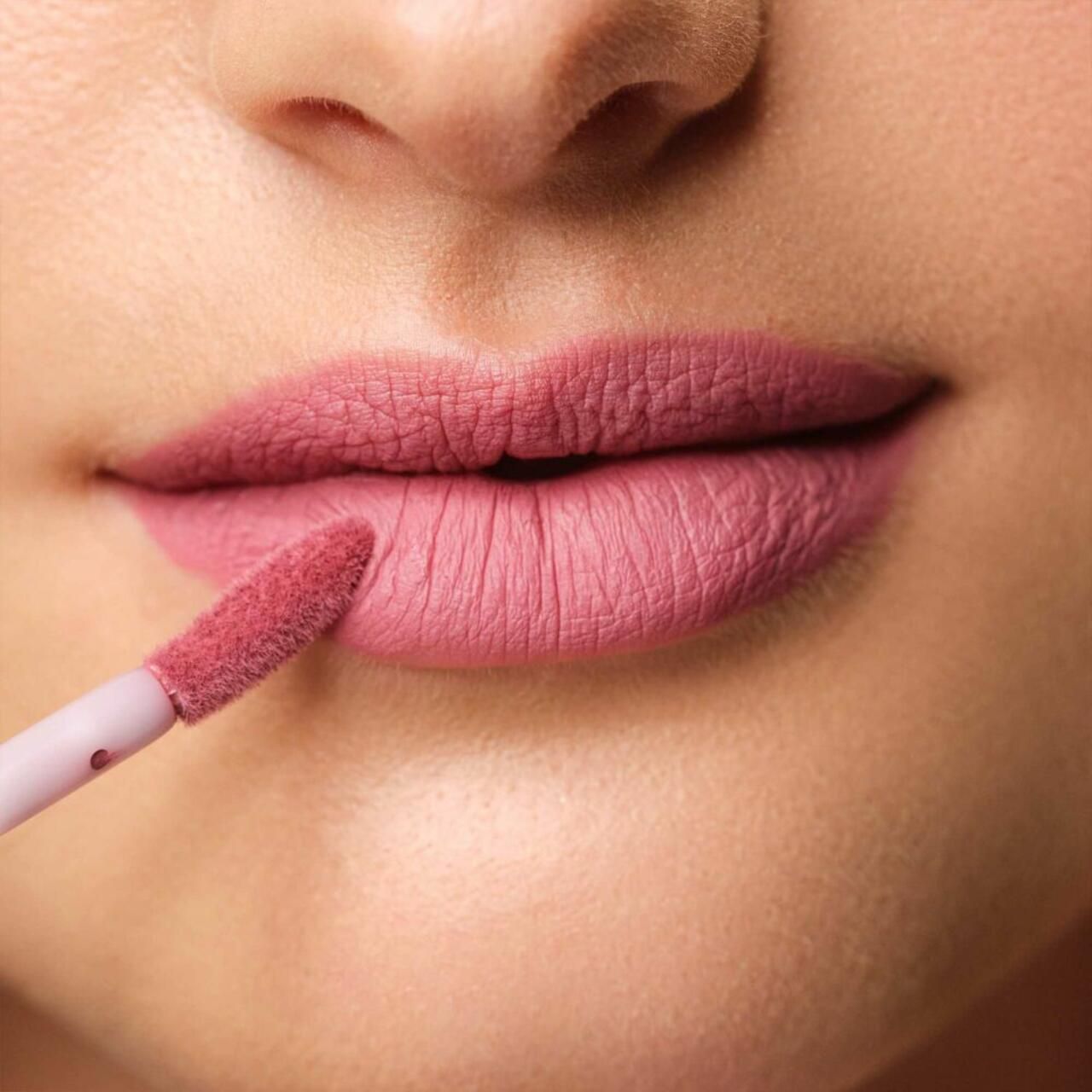 Mund mit aufgetragenem rosa Lippenfluid. Applikator in Gebrauch.