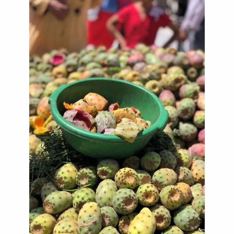 Grüne Schüssel mit Kaktusfrüchten, umgeben von weiteren Früchten. Marktstand.