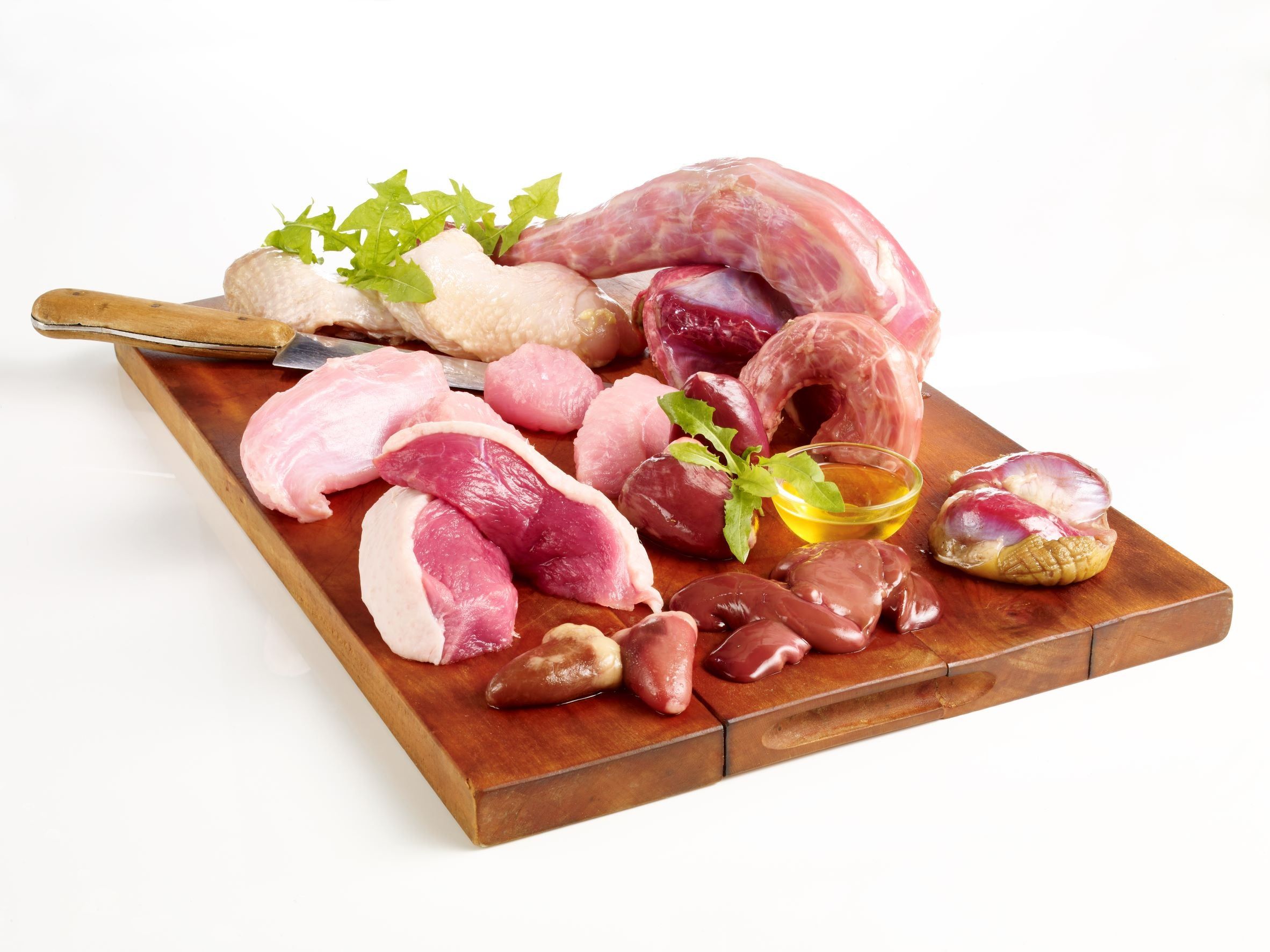 Verschiedene rohe Fleischstücke auf einem Holzbrett. Enthält Geflügel, Innereien und Kräuter.