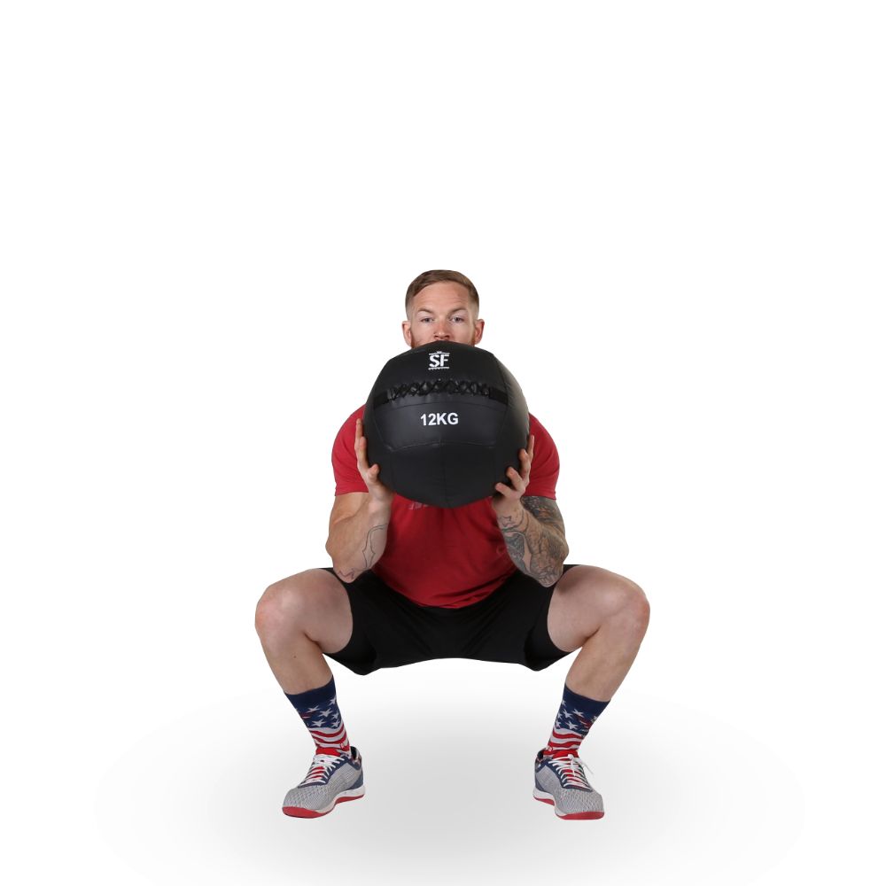 Mann in rotem Shirt hockt mit schwarzem Medizinball. Aufdruck 12KG.