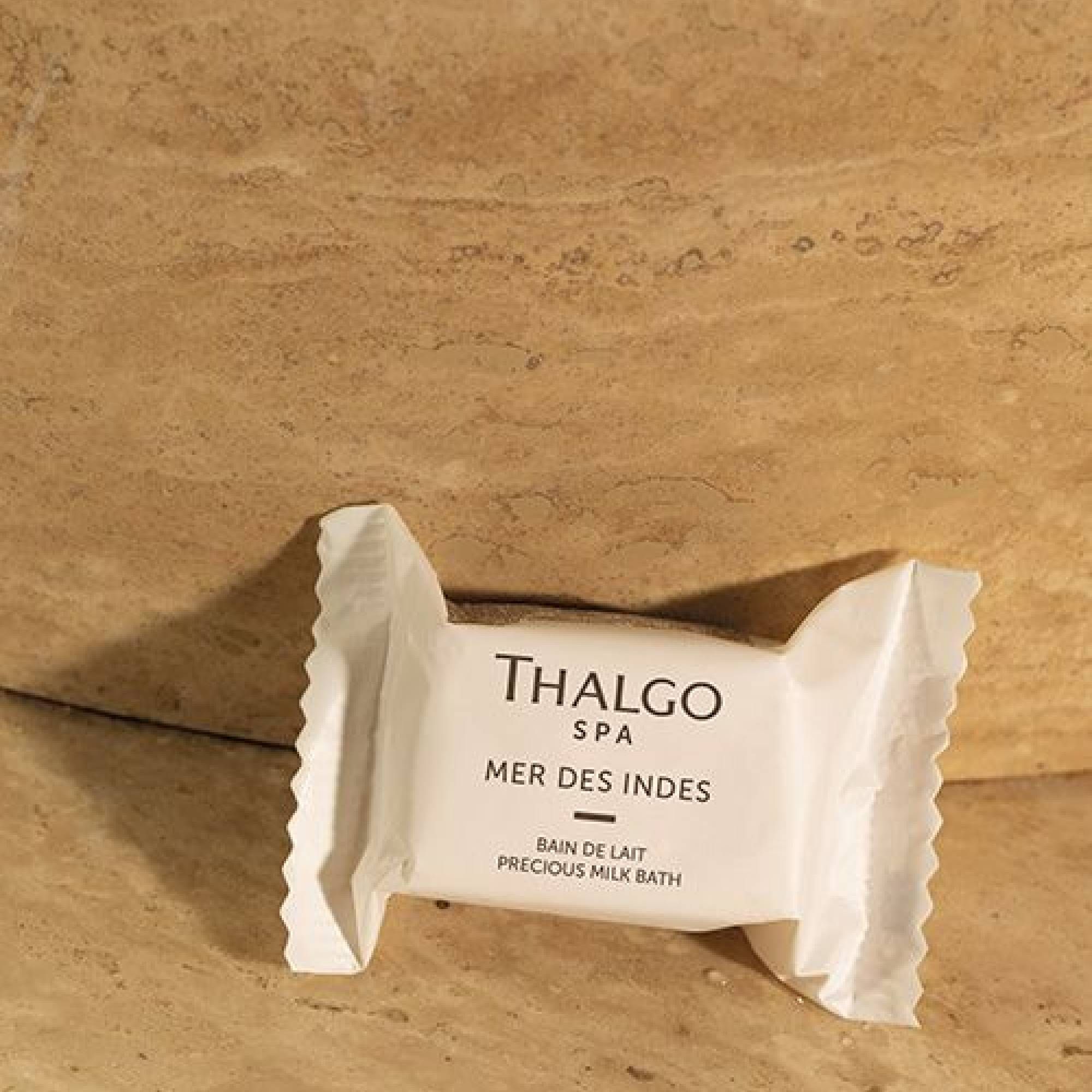 Weißes, rechteckiges Milchbad-Päckchen mit "Thalgo SPA"-Logo und "Mer des Indes"-Schriftzug. "Bain de lait" und "Precious Milk Bath" darunter, auf Steinuntergrund.