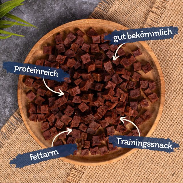 Hölzerner Teller mit quadratischen, braunen Würfeln. Text: proteinreich, fettarm, gut bekömmlich, Trainingssnack.