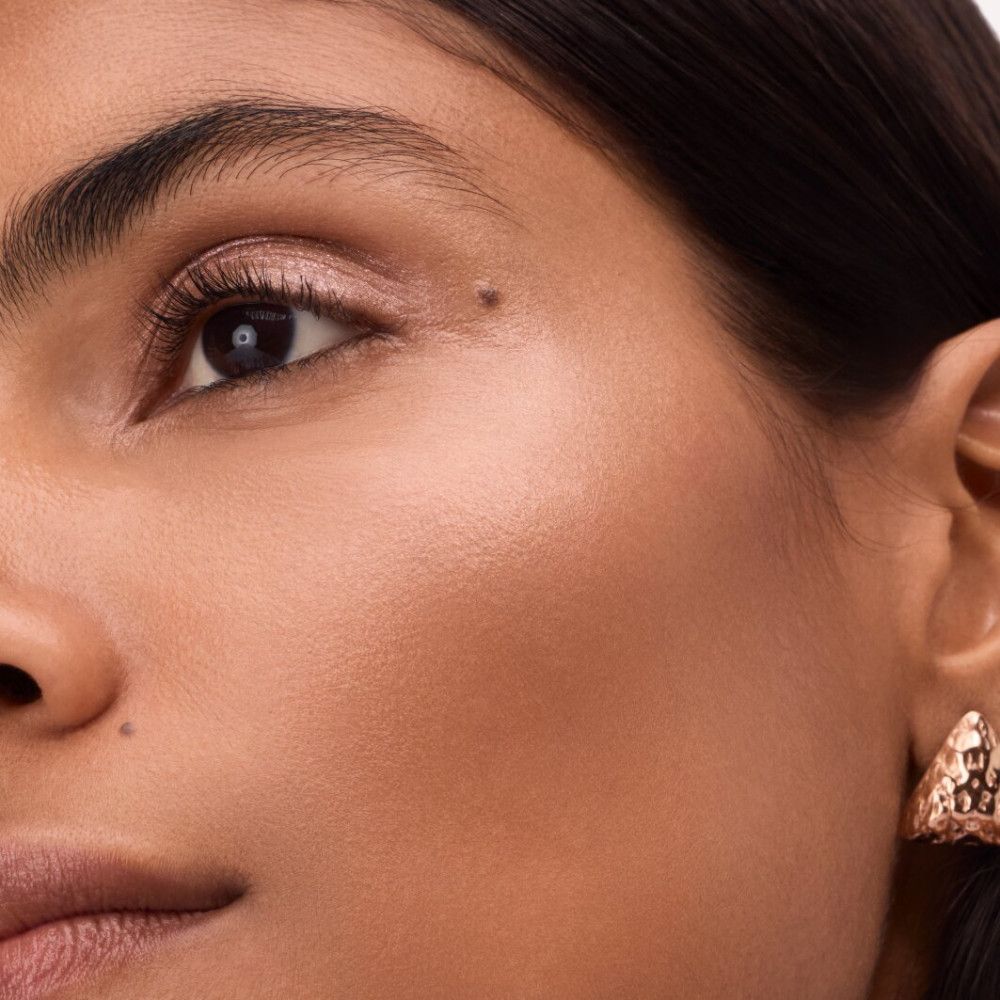 Nahaufnahme eines Gesichts. Highlighter aufgetragen. Goldene Ohrringe.