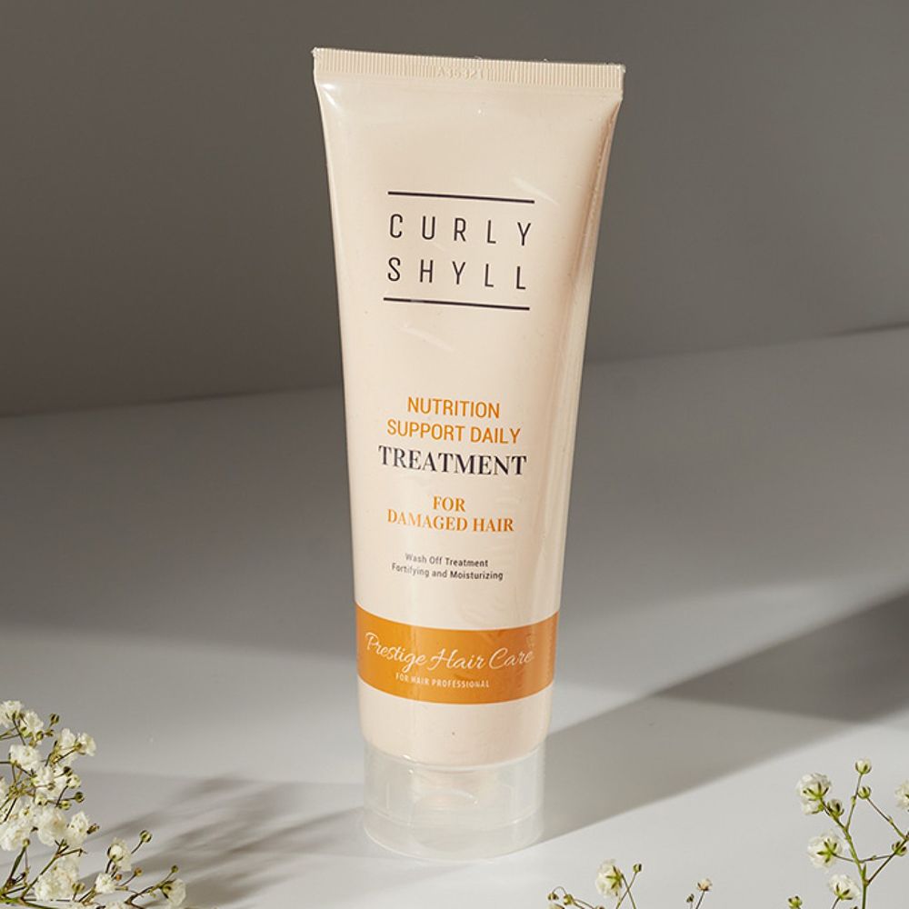Beige Tube mit schwarzer Schrift. Aufschrift: CURLY SHYLL, TREATMENT FOR DAMAGED HAIR. Untertitel: Prestige Hair Care. Weiße Blüten.