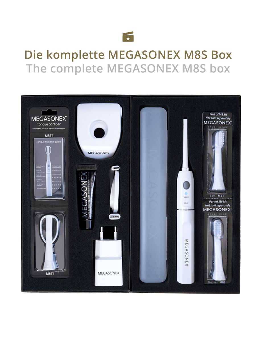 Komplette MEGASONEX M8S Box. Enthält Zahnbürste, Aufsätze, Zungenreiniger, Ladegerät, Reiseetui und Zahnpasta. Schwarze Verpackung.
