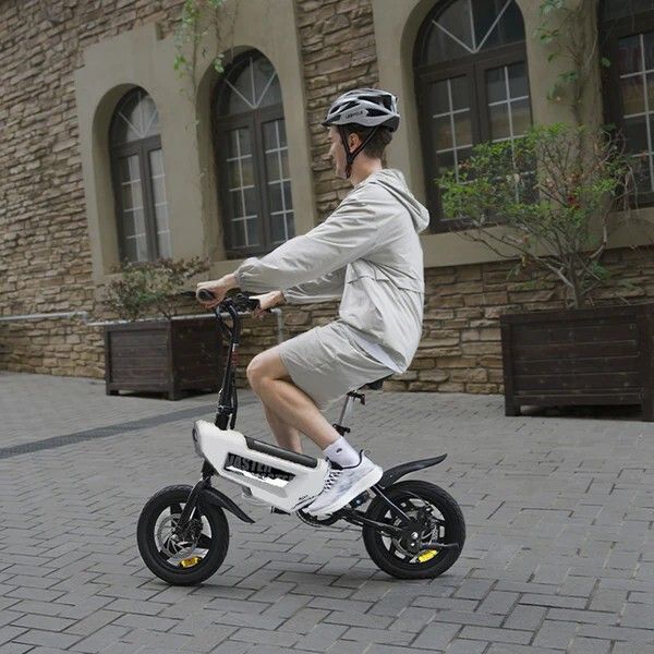 Person fährt auf einem weißen und schwarzen faltbaren E-Bike. Trägt Helm. Hintergrund: Straße, Gebäude.