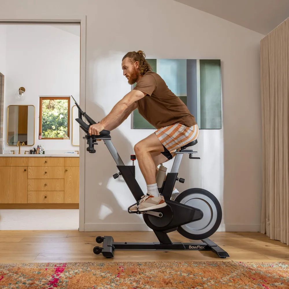 Ein Mann trainiert auf einem Ergometer. Er trägt Sportkleidung und trainiert in einem hellen Raum. Der Ergometer ist schwarz.