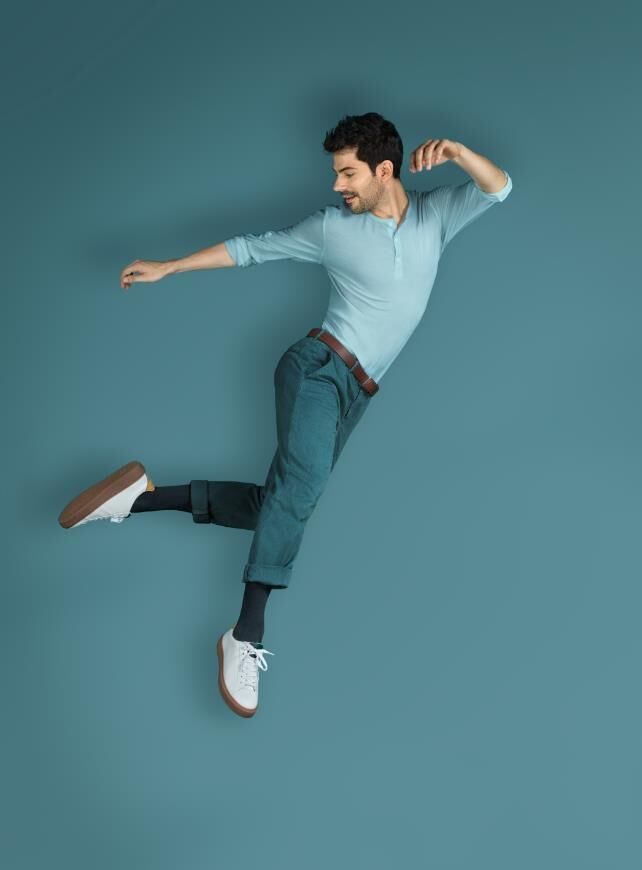 Mann in hellblauem Hemd und Jeans, mit schwarzen Socken und weißen Schuhen. Er springt.