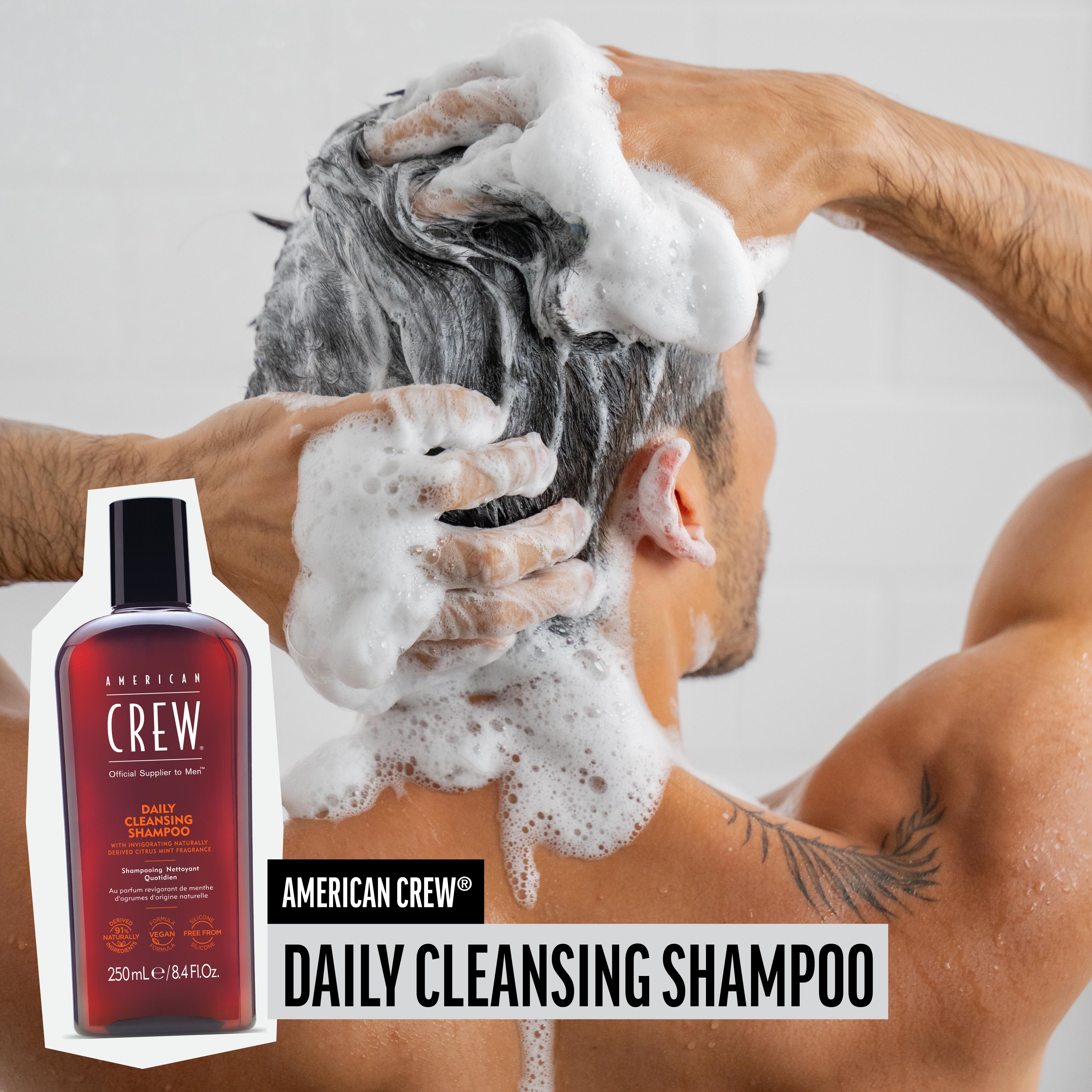 Mann wäscht sich die Haare mit Schaum. AMERICAN CREW Daily Cleansing Shampoo-Flasche im Bild.