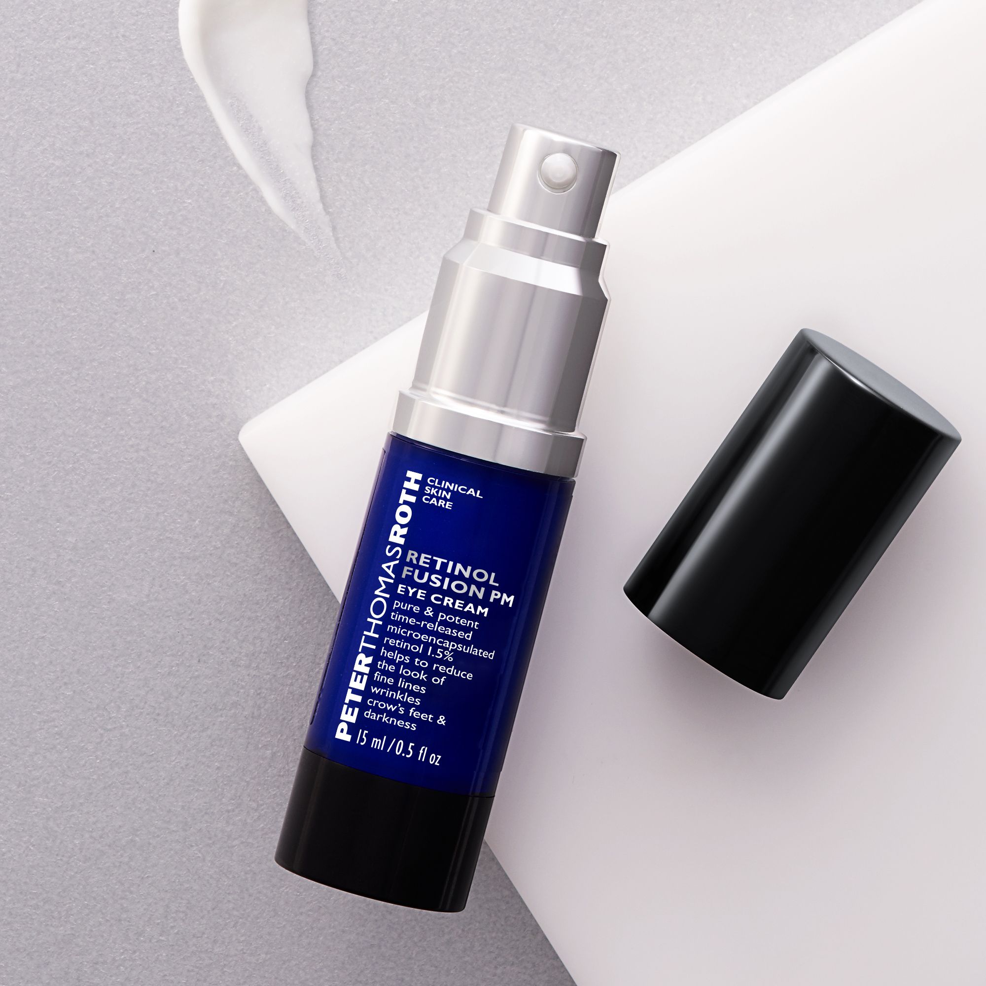 Blau-silberne Flasche mit schwarzem Deckel. Aufschrift: Retinol Fusion PM Eye Cream. Volumen: 15 ml/0,5 fl oz. Deckel daneben.