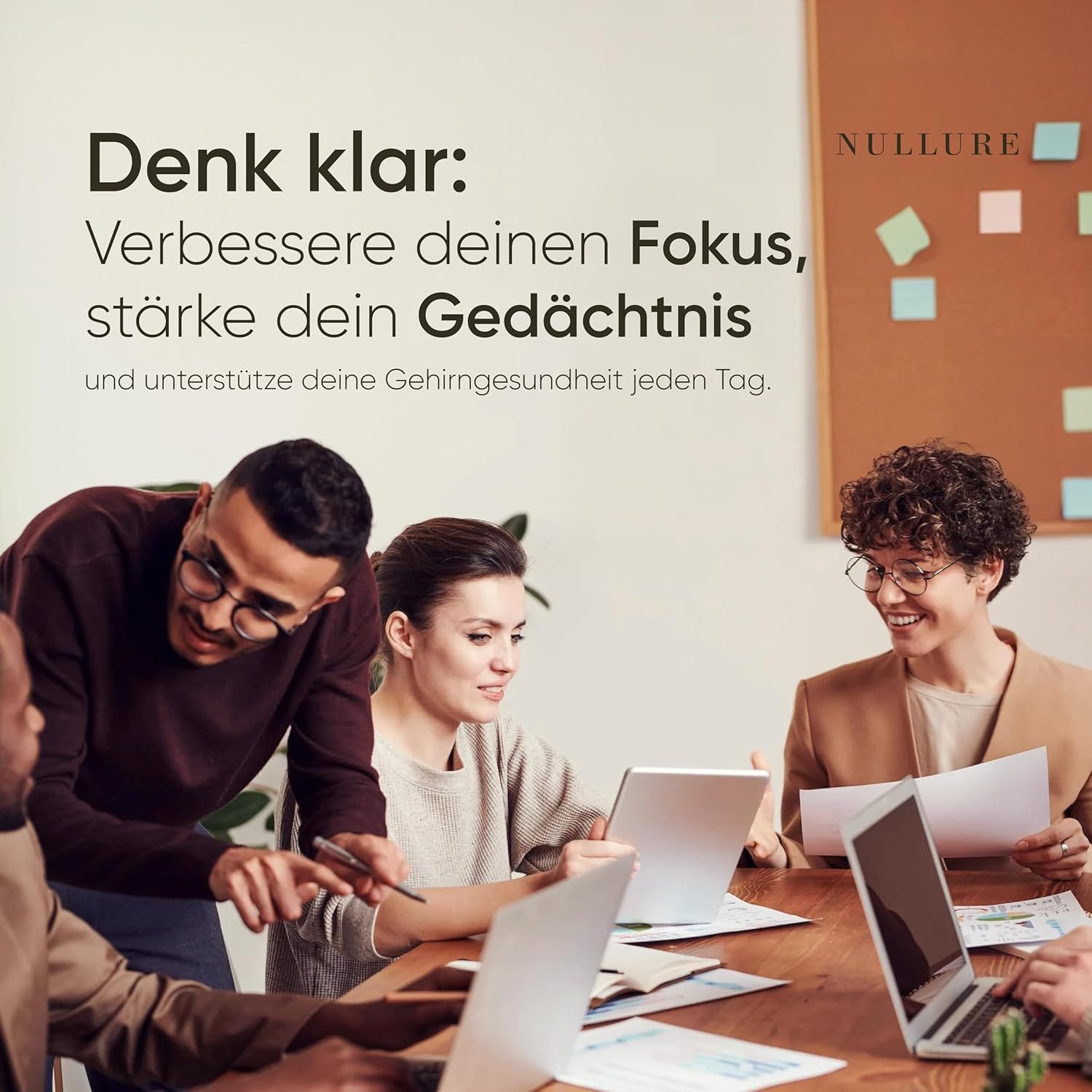 Büro-Szene. Menschen sitzen an einem Tisch mit Laptops und Tablets. Eine Person zeigt auf ein Tablet. Auf einem Pinnwand: Nullure.
