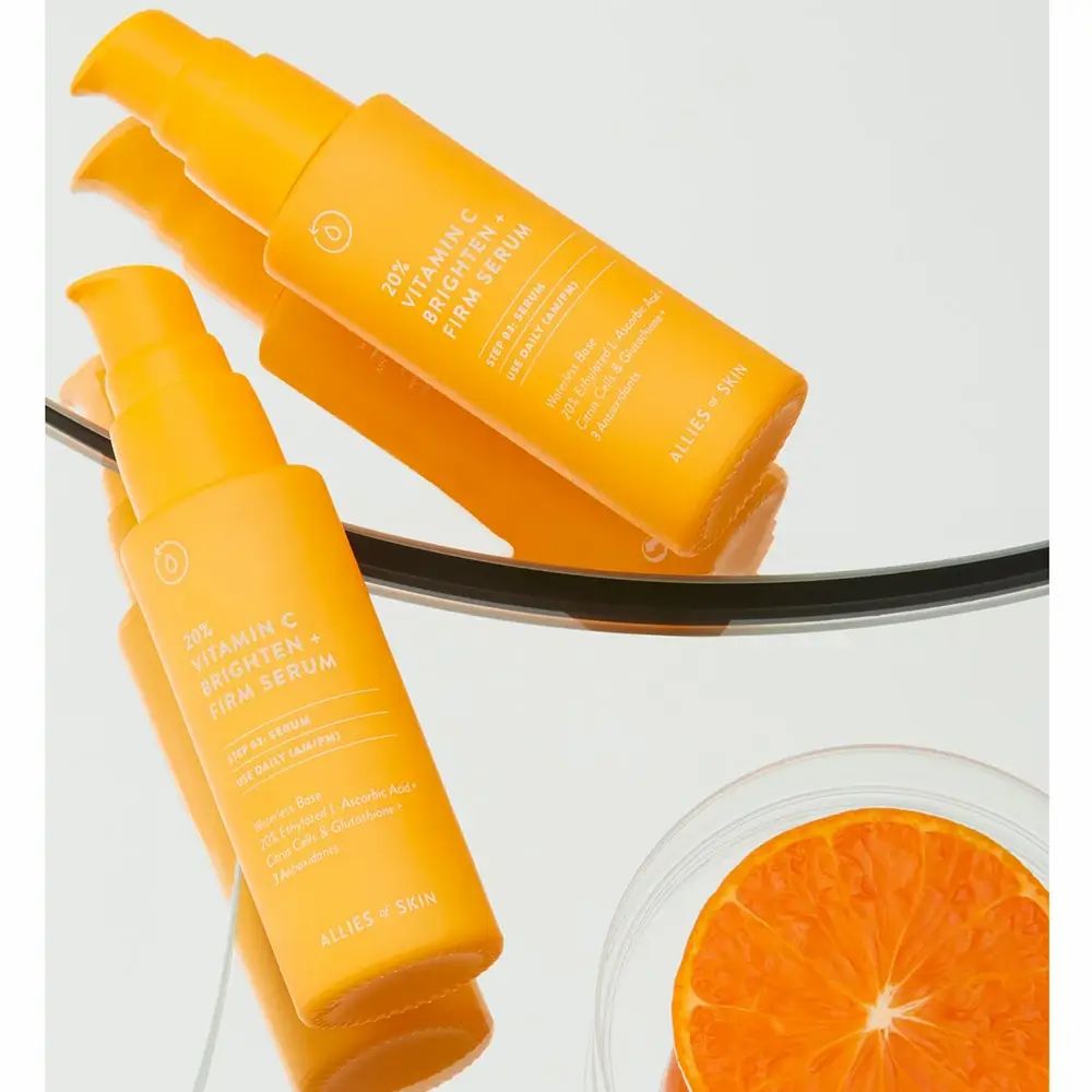 Zwei gelbe Flaschen mit Dosierpumpe. Aufschrift: 20% Vitamin C Brighten + Firm Serum. Marke: ALLIES OF SKIN. Spiegelung auf einer Oberfläche.