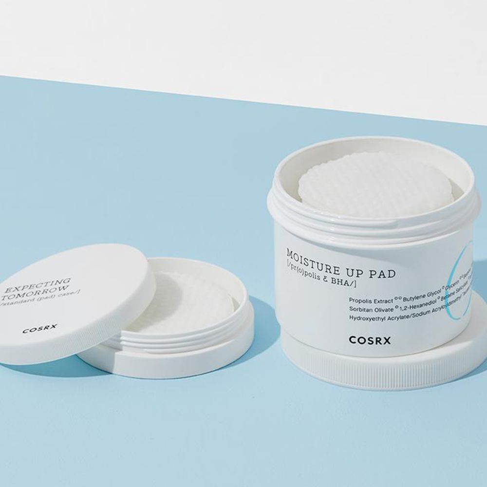 Geöffnete weiße Dose mit Pads. Deckel daneben. Text: "MOISTURE UP PAD" und "COSRX".