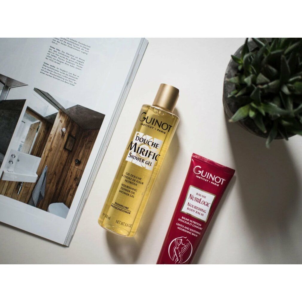 Guinot Mirific Shower Gel und Nourishing Body Balm. Gelbe Flasche, rote Tube. Auf weißem Untergrund mit Magazin und Pflanze.