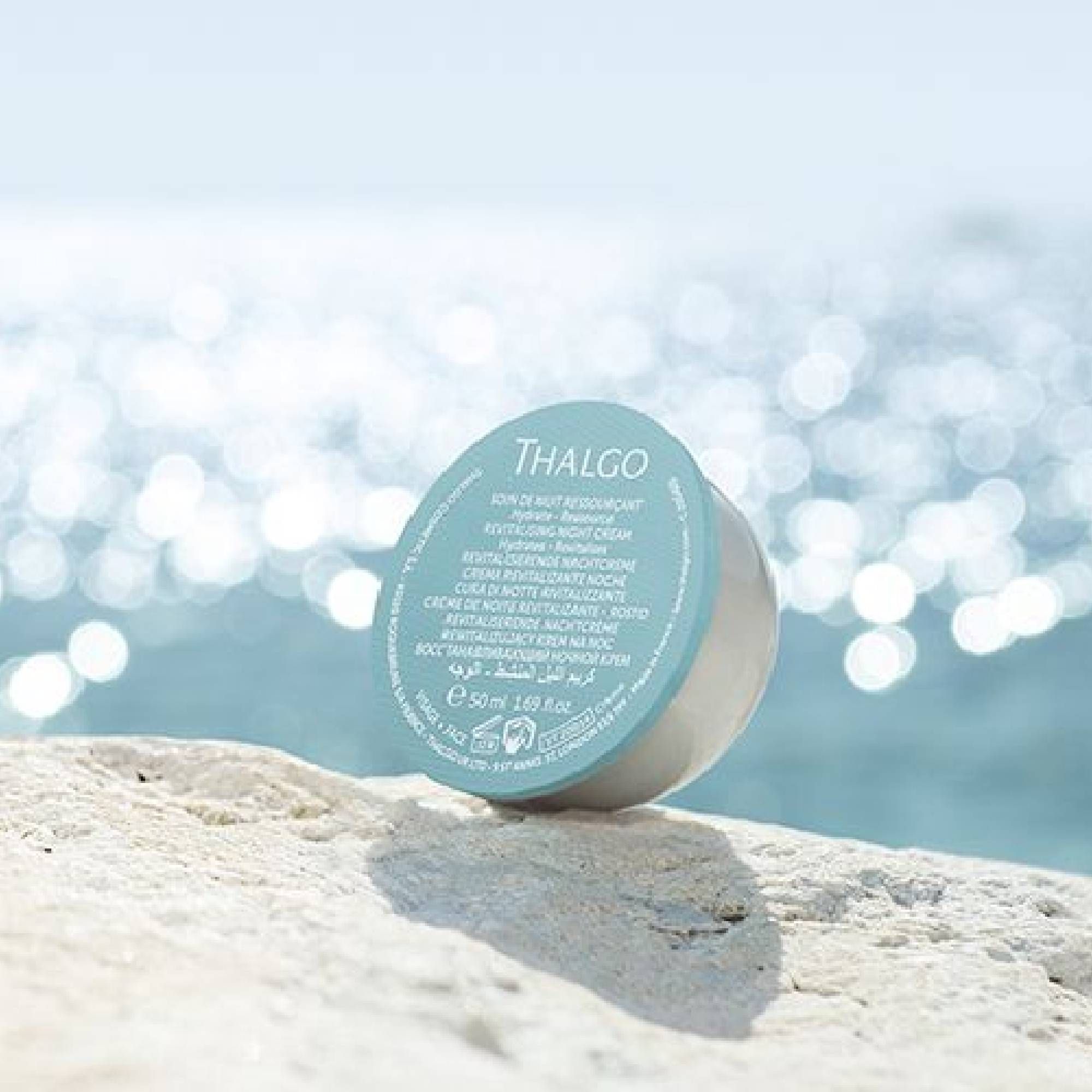 Creme-Verpackung mit blauem Deckel, THALGO-Logo. Vor blauem Wasser und Felsen platziert.