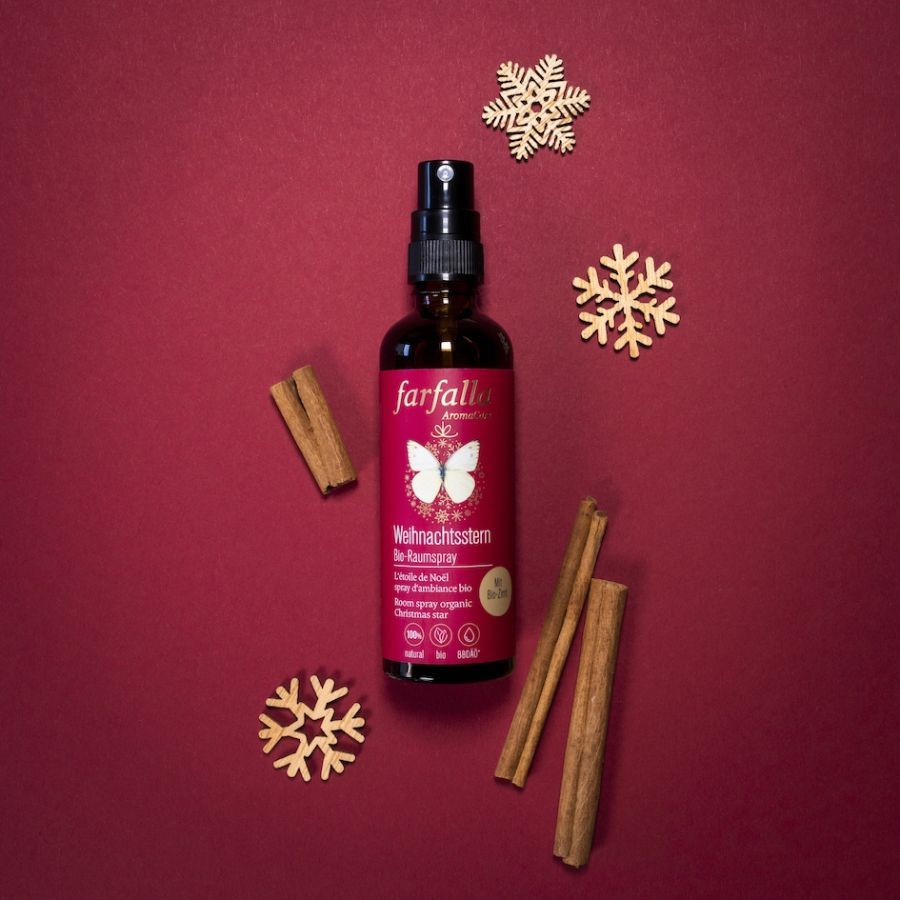 Braune Glasflasche mit Sprühkopf. Rotes Etikett mit weißem Schmetterling und Text. Zimtstangen und Holzsterne liegen daneben.