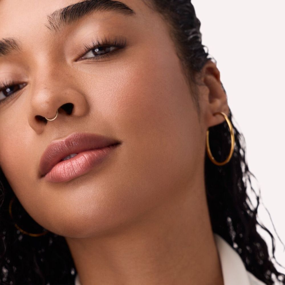 Nahaufnahme eines Gesichts mit Lippen, die mit einem glänzenden Produkt bedeckt sind. Goldener Nasenring.