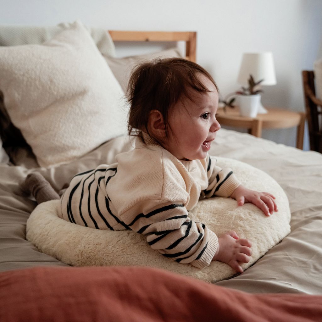 Baby liegt auf einem Bett, auf einem cremefarbenen Kissen. Baby trägt gestreifte Kleidung.