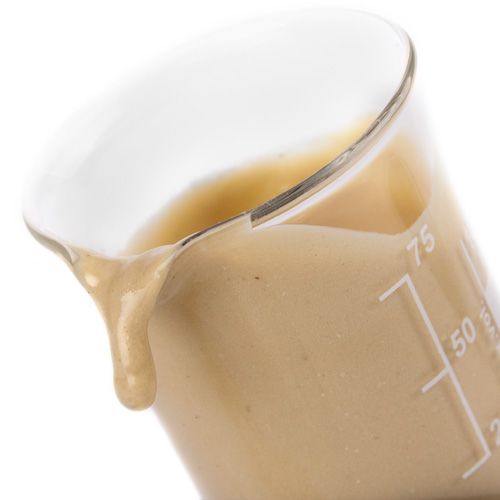 Becherglas mit pastöser, beiger Substanz. Flüssigkeit tropft aus dem Glas.