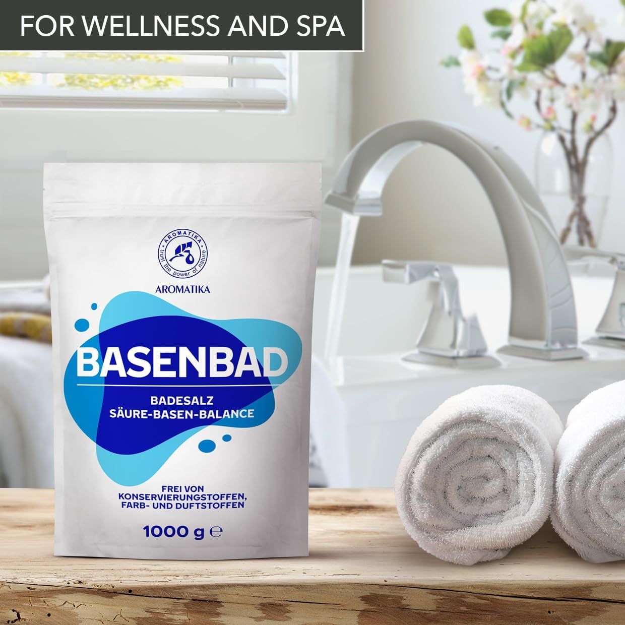 Weiße Verpackung mit blauem Design. BASENBAD, Badesalz, Säure-Basen-Balance. Logo: AROMATIKA. Wasserhahn, Handtücher. Text: Frei von Konservierungsstoffen, Farb- und Duftstoffen. 1000 g.