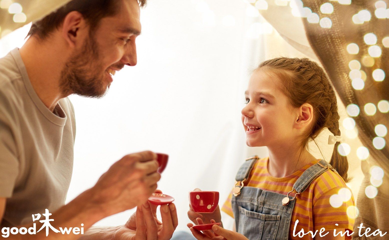 Vater und Tochter trinken Tee aus roten Tassen. Logo "goodwei" und Schriftzug "love in tea" sichtbar.