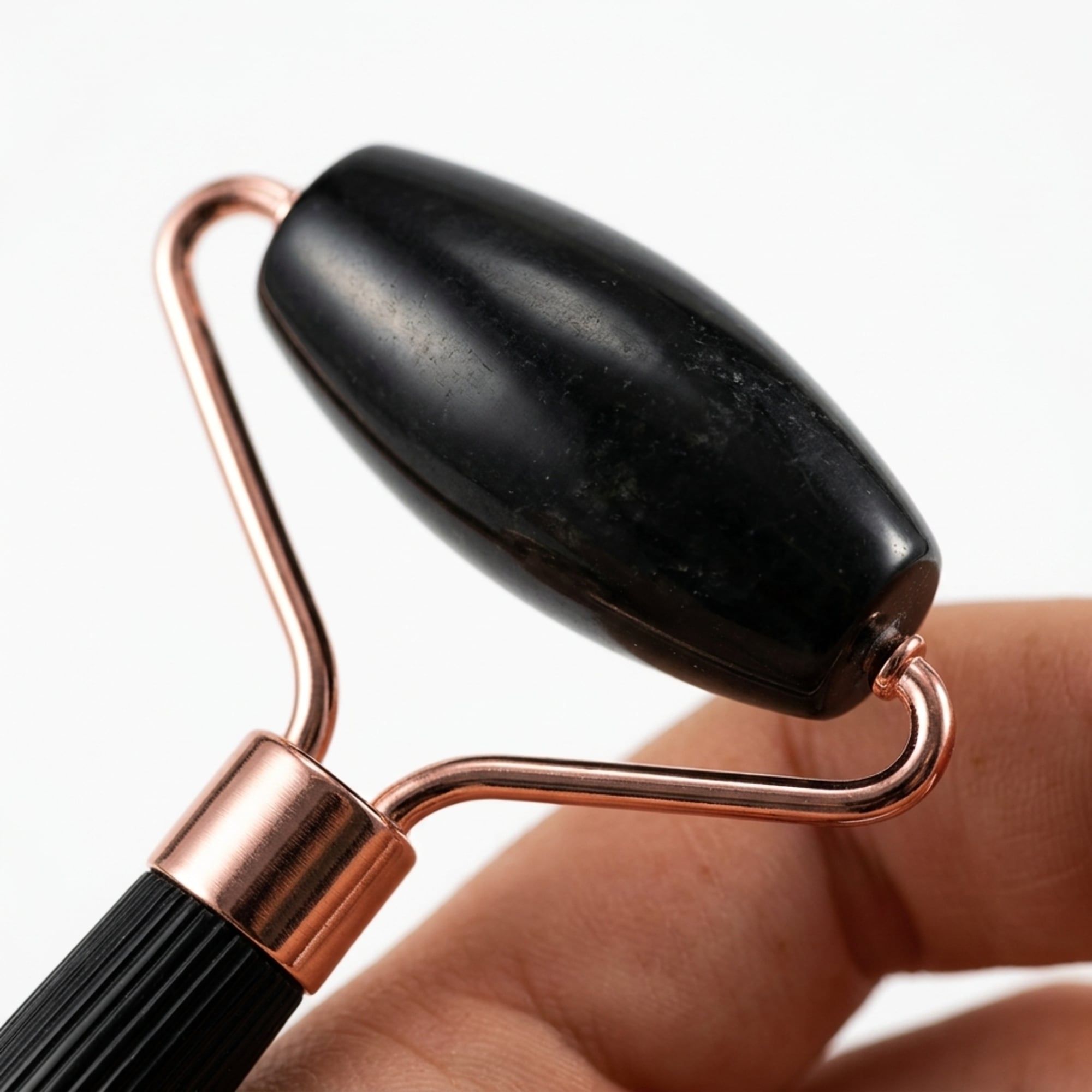 Schwarzer Jade-Roller mit kupferfarbenem Metallrahmen, gehalten von einer Hand.