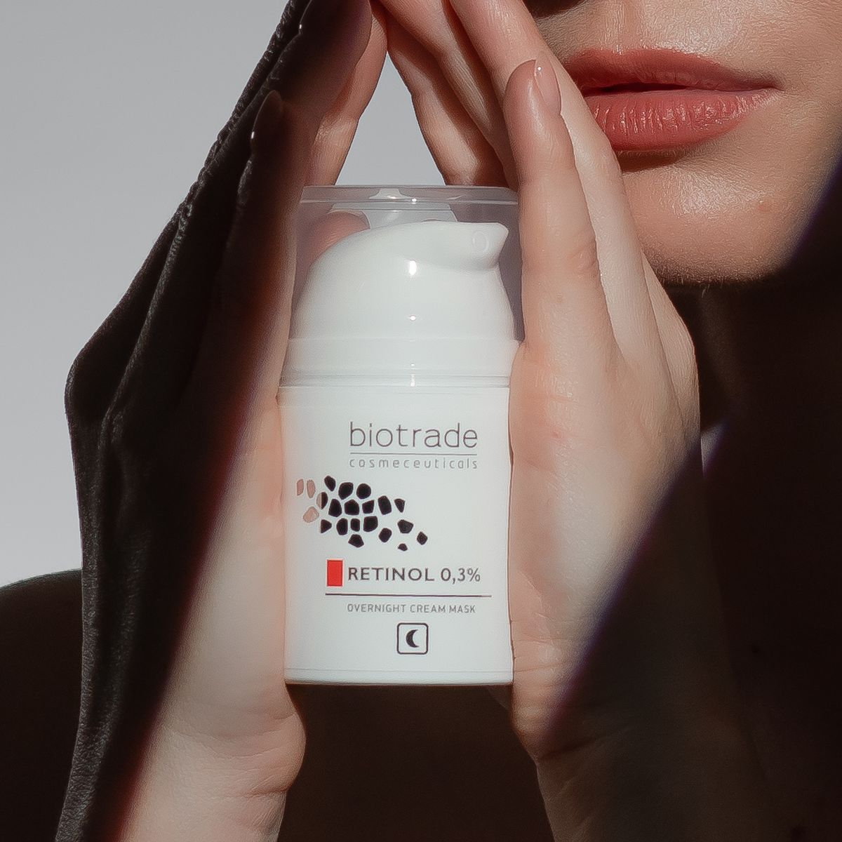 Weiße Flasche mit Aufschrift Biotrade, Retinol 0,3% und Nachtcreme-Gesichtsmaske. Hände halten die Flasche.