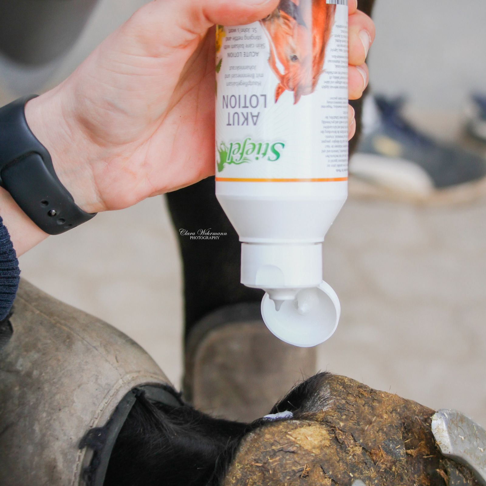 Person hält eine Flasche Stiefel Akutlotion. Die Flasche hat einen weißen Deckel und einen weißen Körper. Auf der Flasche ist ein Etikett.