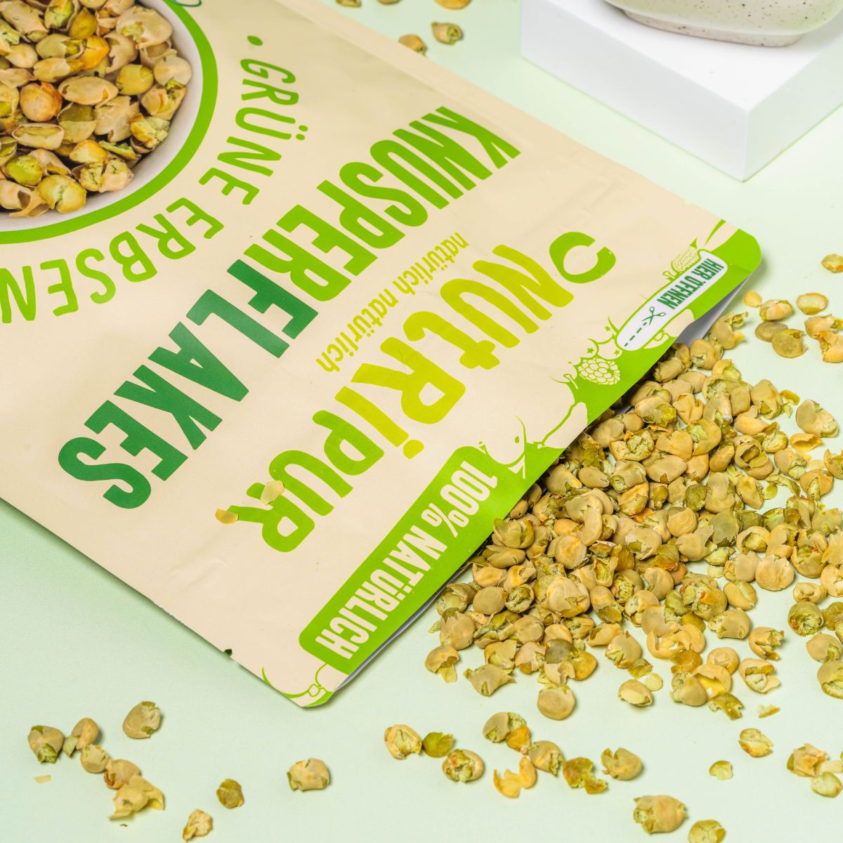 Verpackung von NutriPur Grüne Erbsen Knusperflakes. Aufschrift: Knusperflakes, Grüne Erbsen, 100% natürlich. Flakes verstreut.