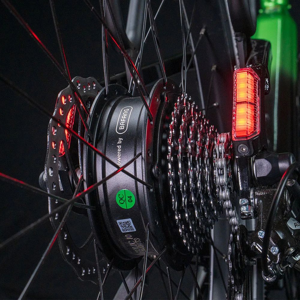 Nahaufnahme des Hinterrads. Rote Reflektoren, Scheibenbremse und Kette. Aufschrift: Powered by Bafang.