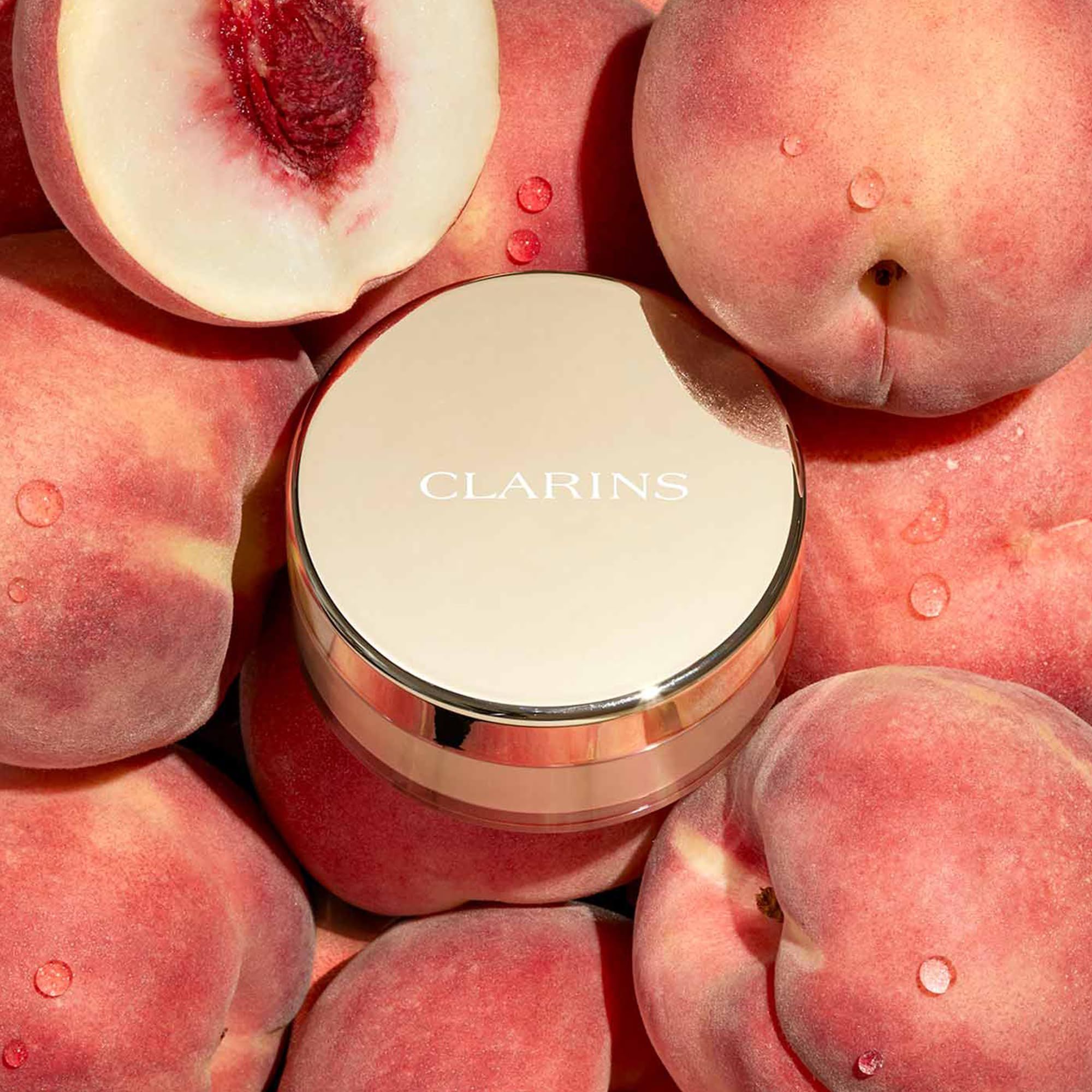 Clarins Ever Matte Loose Powder, Farbton 01. Goldfarbener Behälter, umgeben von Pfirsichen.