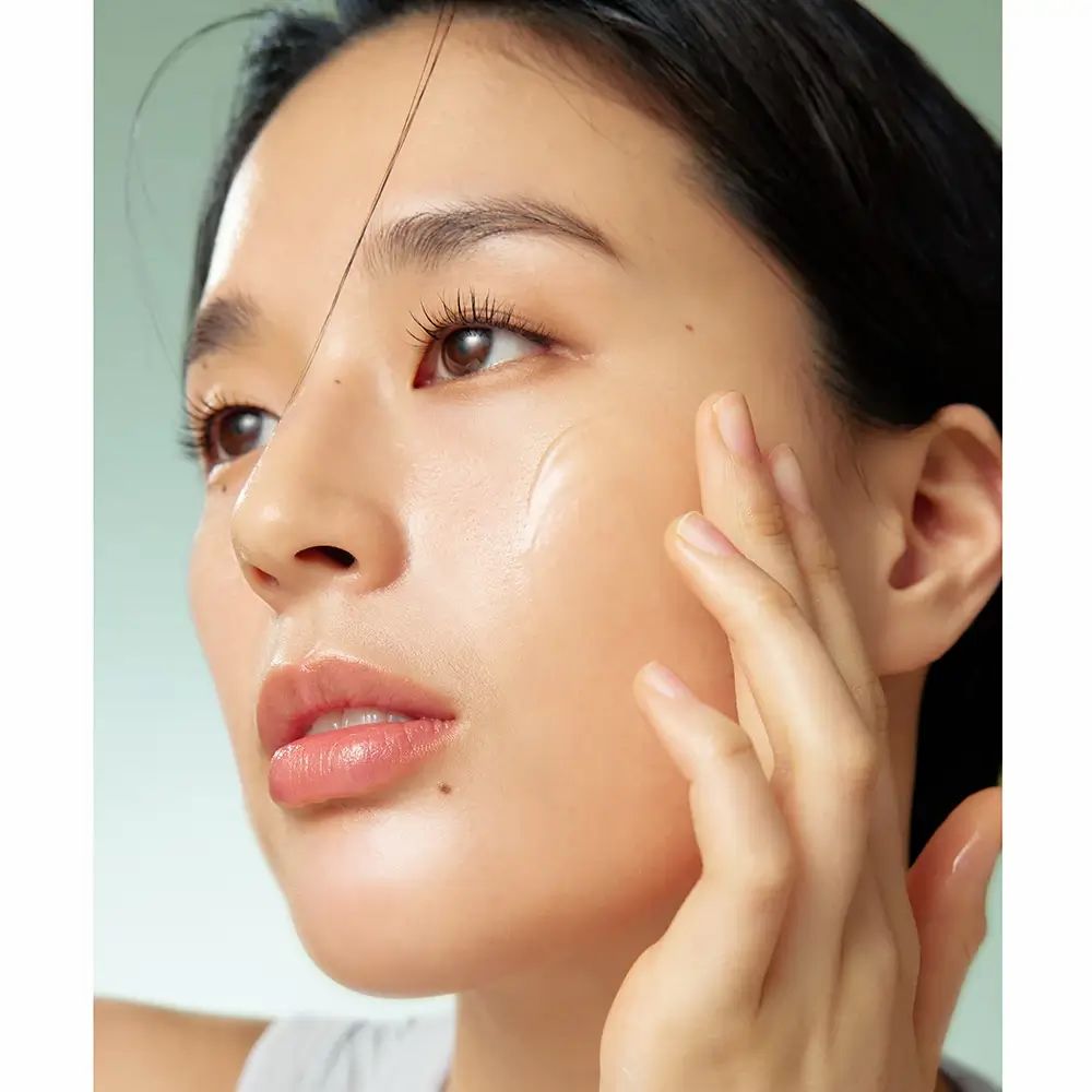 Nahaufnahme einer Person, die Serum auf ihr Gesicht aufträgt. Helle Haut, Serum auf der Haut sichtbar. Helle Umgebung.