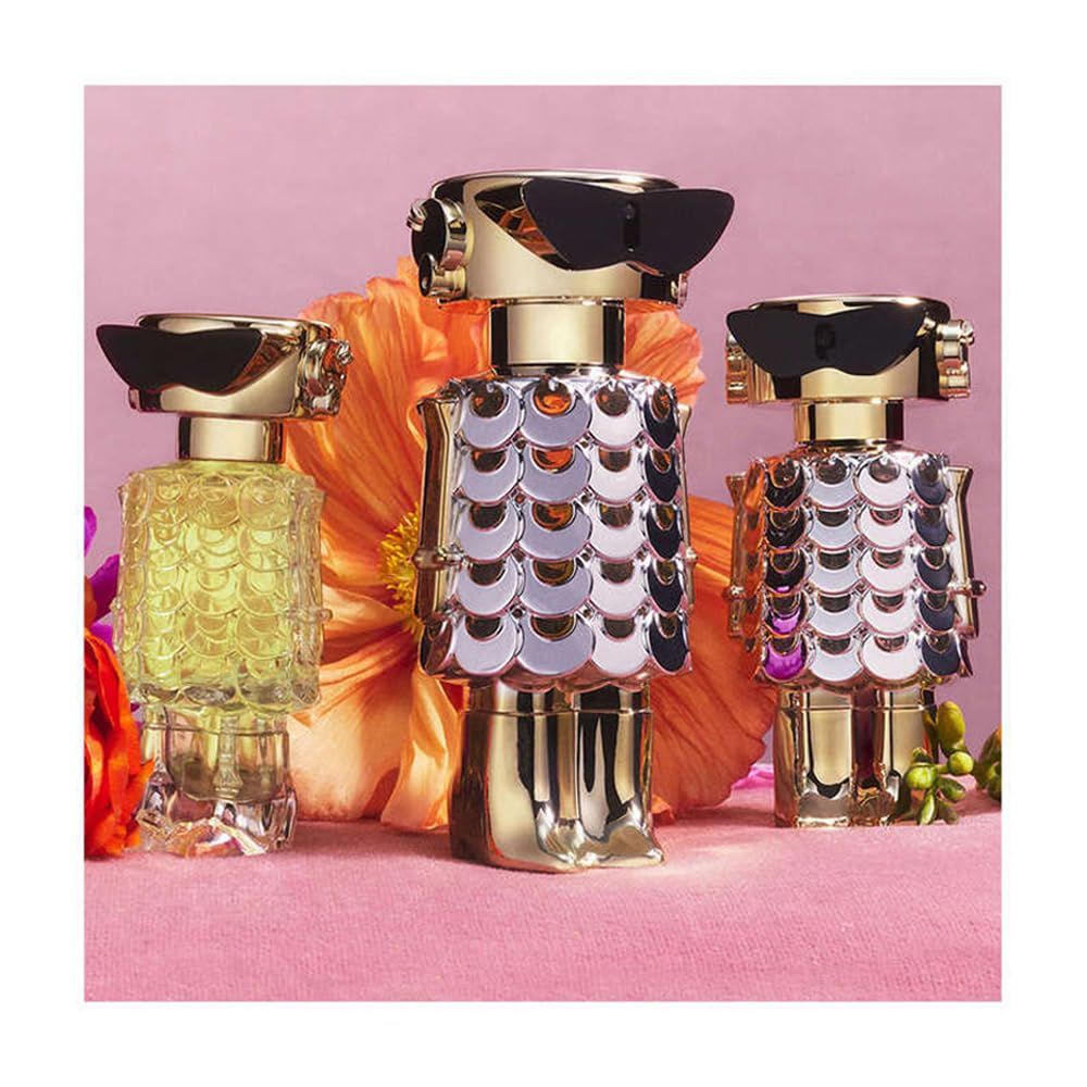 Drei Roboter-Parfümflakons. Gold, silberne Schuppen, schwarze Brillen. Blumen im Hintergrund.