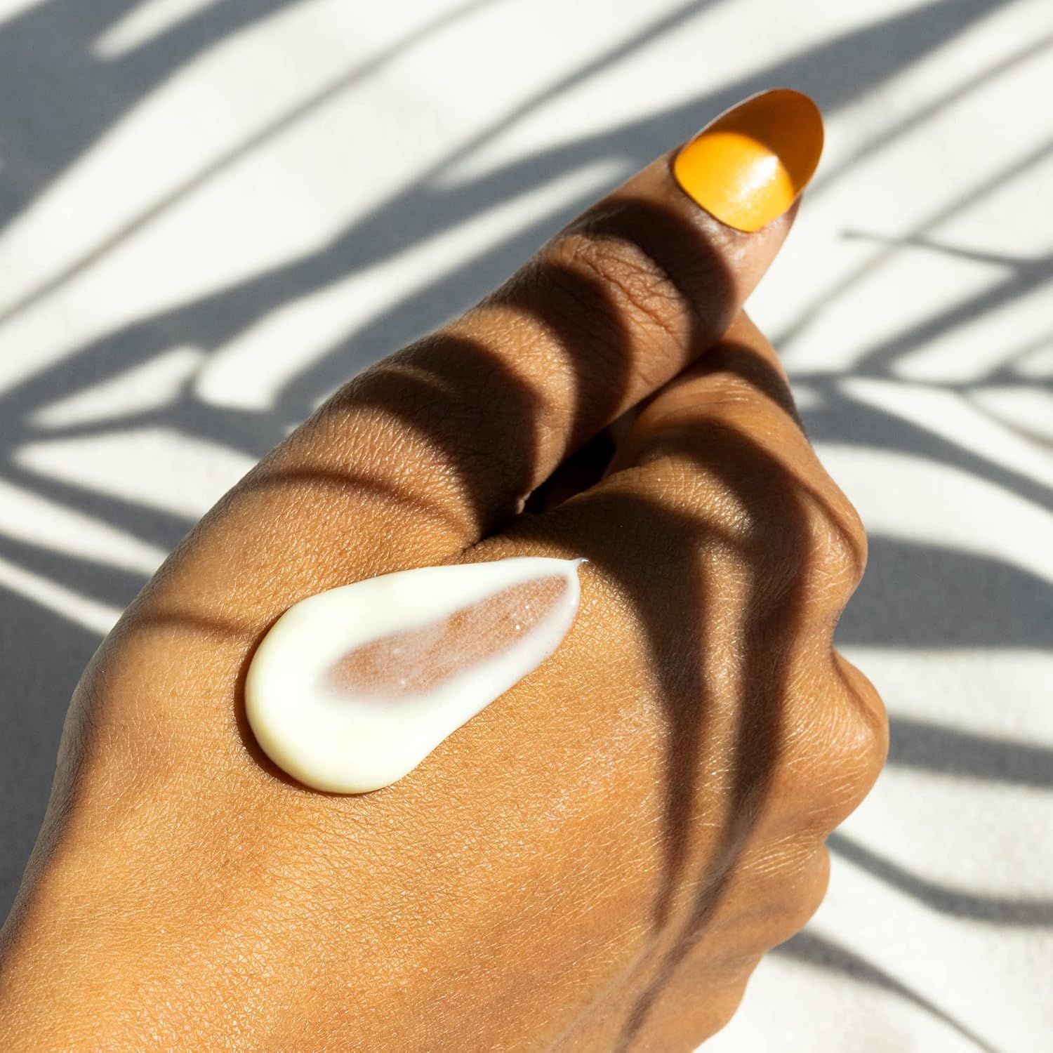 Hand mit einem Tupfer weißer Creme auf dem Handrücken, mit gelbem Nagellack.