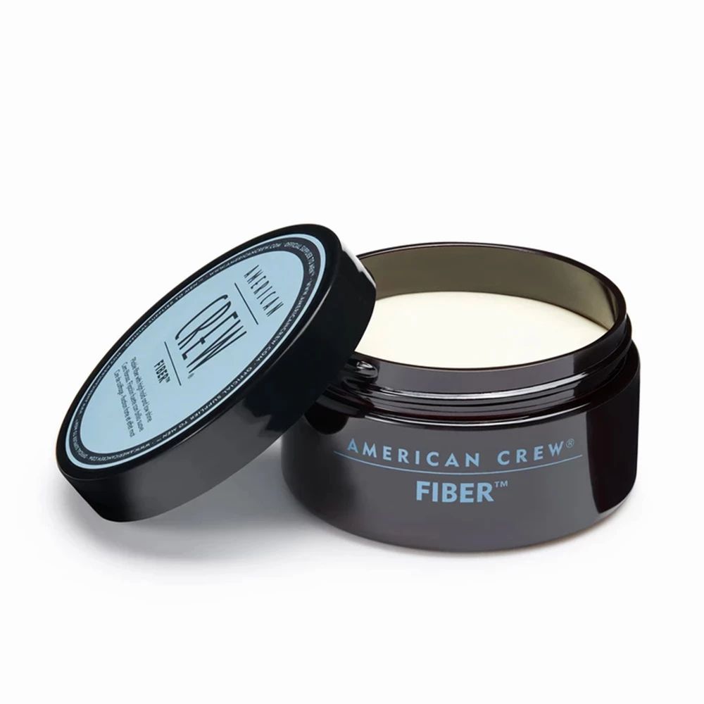 Geöffnete, dunkelblaue Dose mit "AMERICAN CREW FIBER"-Aufschrift. Cremefarbene Haarcreme sichtbar.