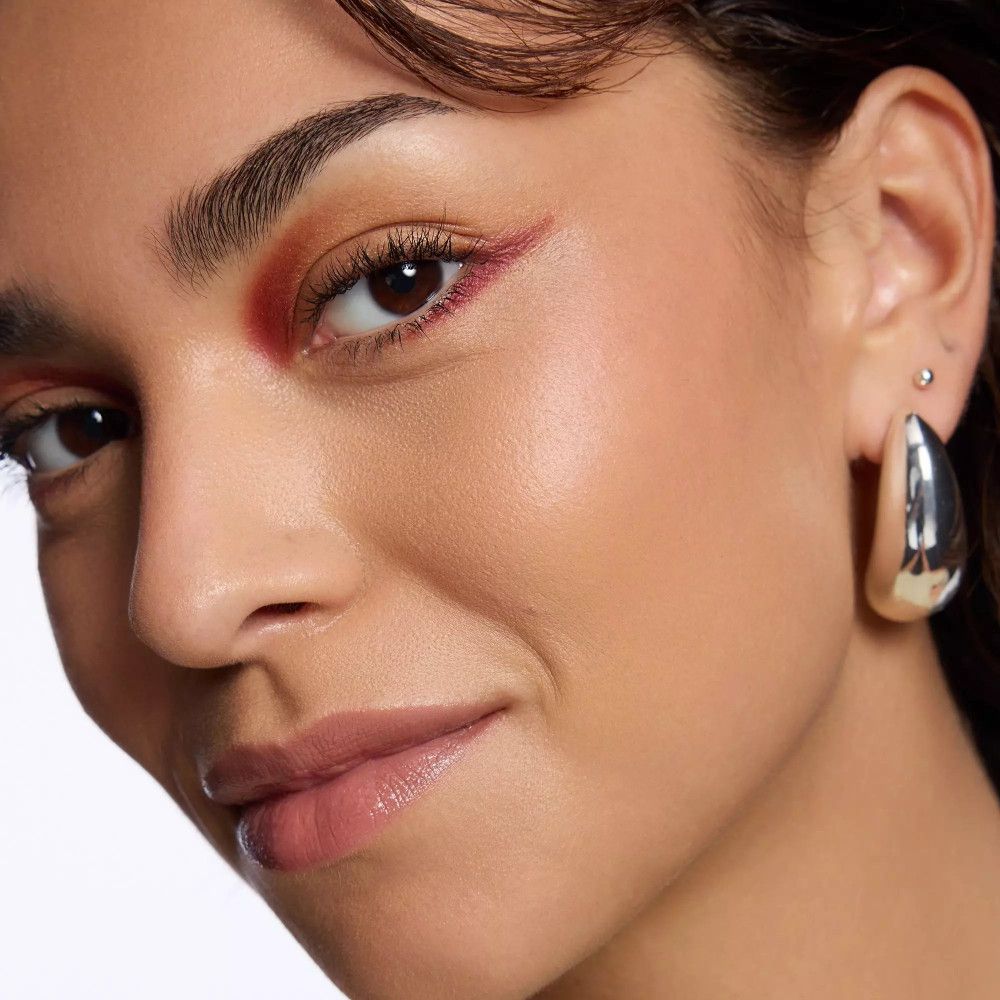 Nahaufnahme einer Frau mit rosafarbenem Lidschatten. Goldene Ohrringe.