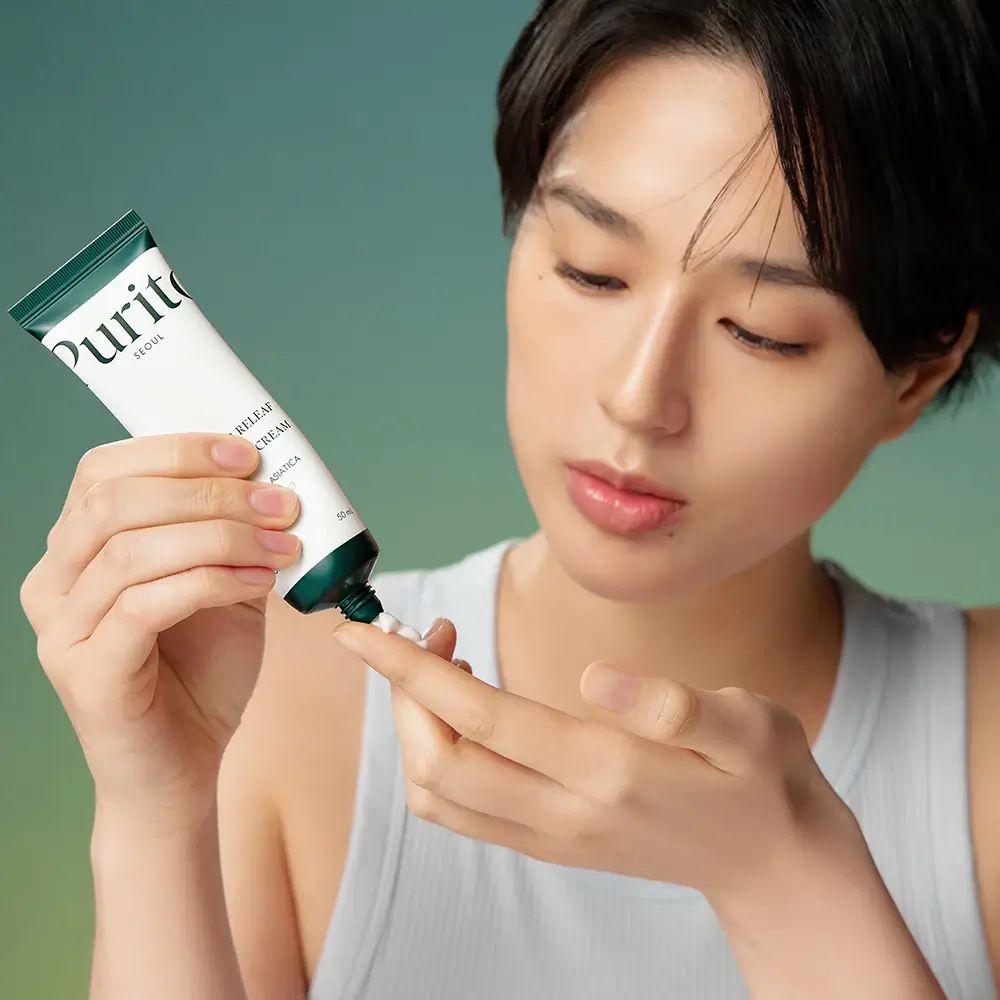 Frau drückt Creme aus einem Tube auf ihren Finger. Aufschrift: PURITO, Wonder Releaf Centella Cream.