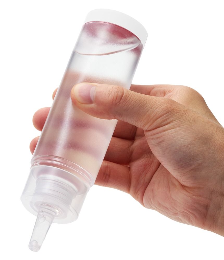 Hand hält eine transparente Flasche mit rotem Deckel. Flüssigkeit sichtbar. Ausgießer an der Spitze.