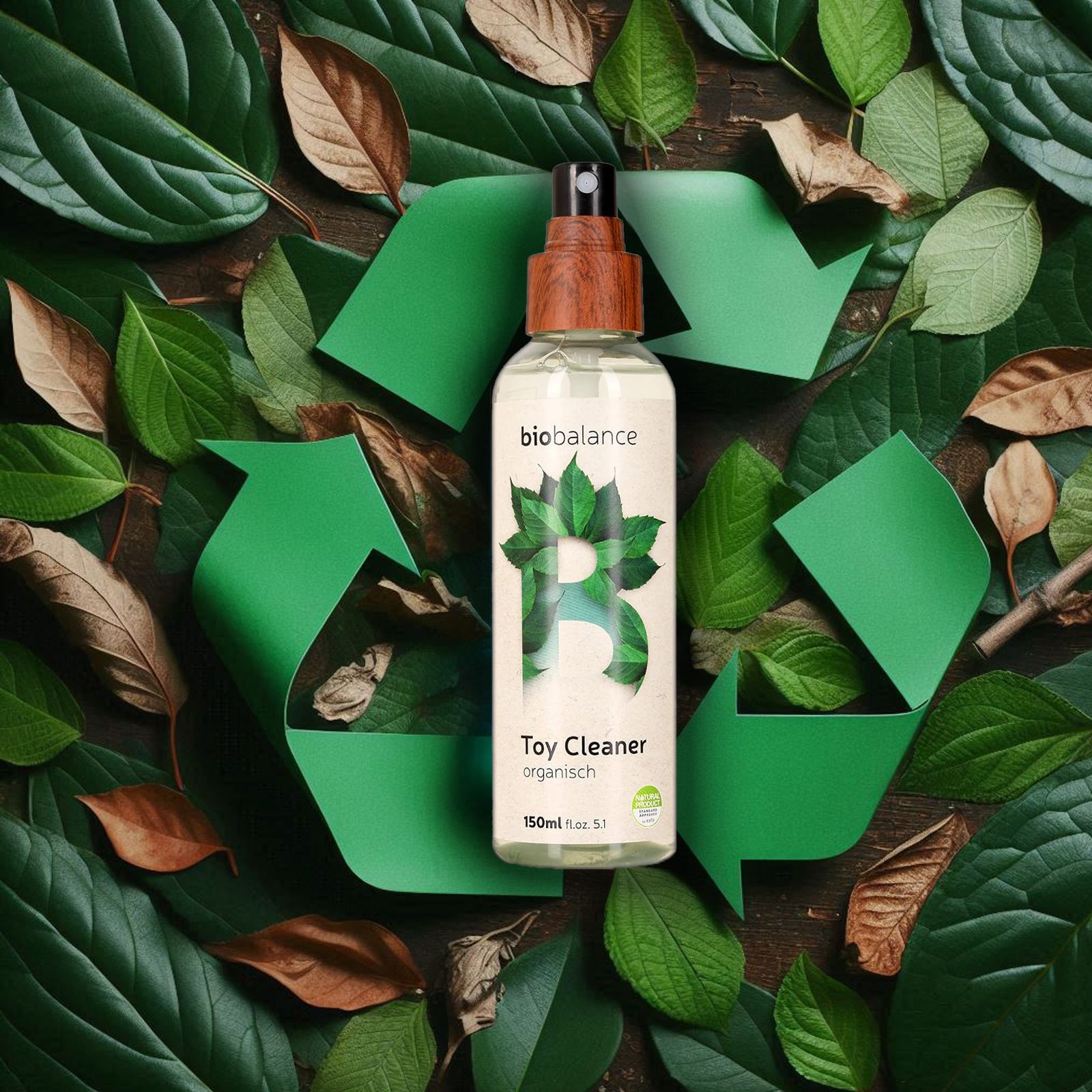 BIO BALANCE Toy Cleaner, organisch. Flasche mit Holz-Sprühkopf, umgeben von Blättern und Recycling-Symbol.
