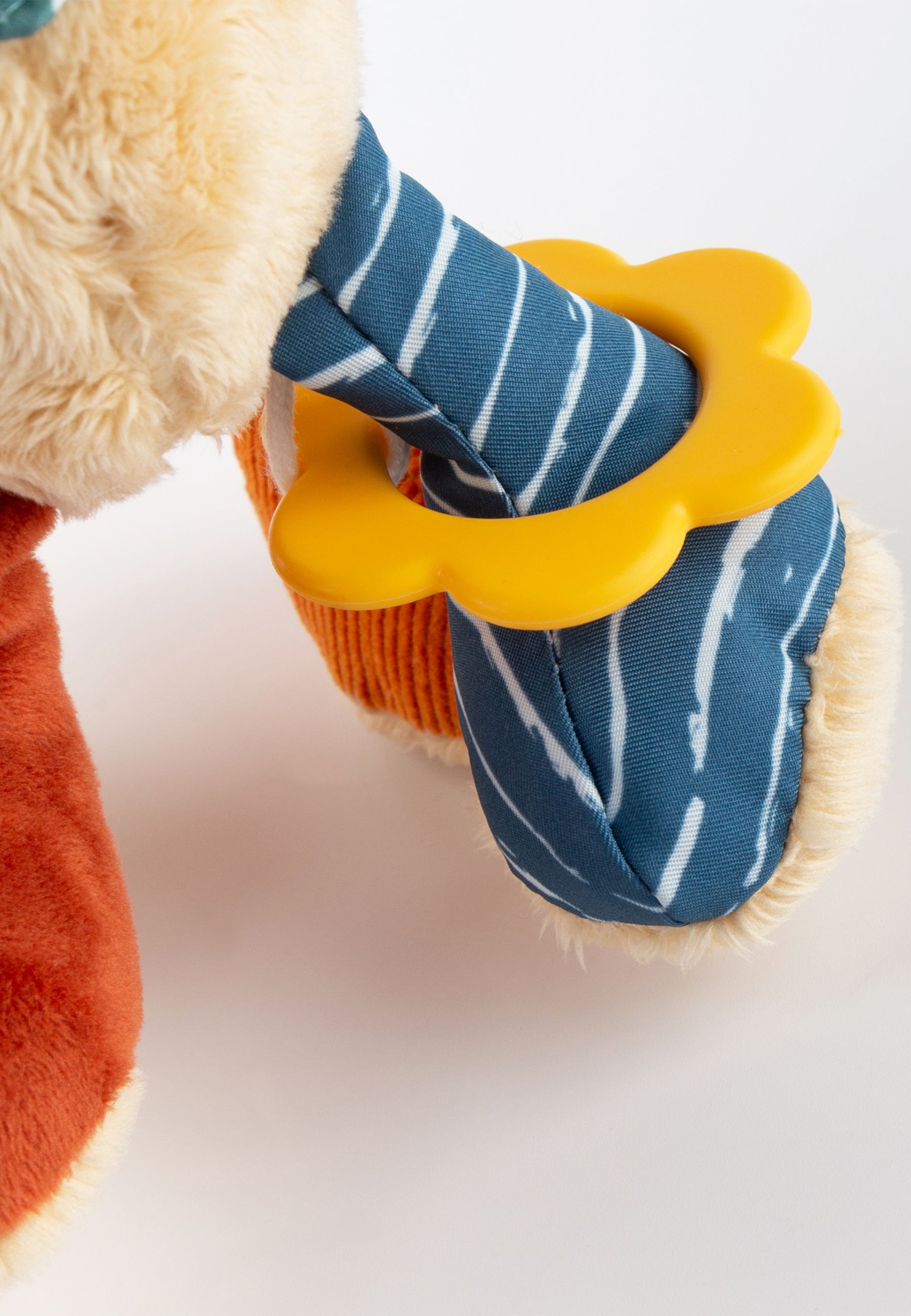 Detailaufnahme des Stoffhundes mit gelbem Ring an blau-weiß gestreifter Pfote. Orangefarbene Pfote.