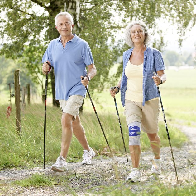Zwei ältere Menschen beim Nordic Walking. Eine Person trägt eine Kniebandage.