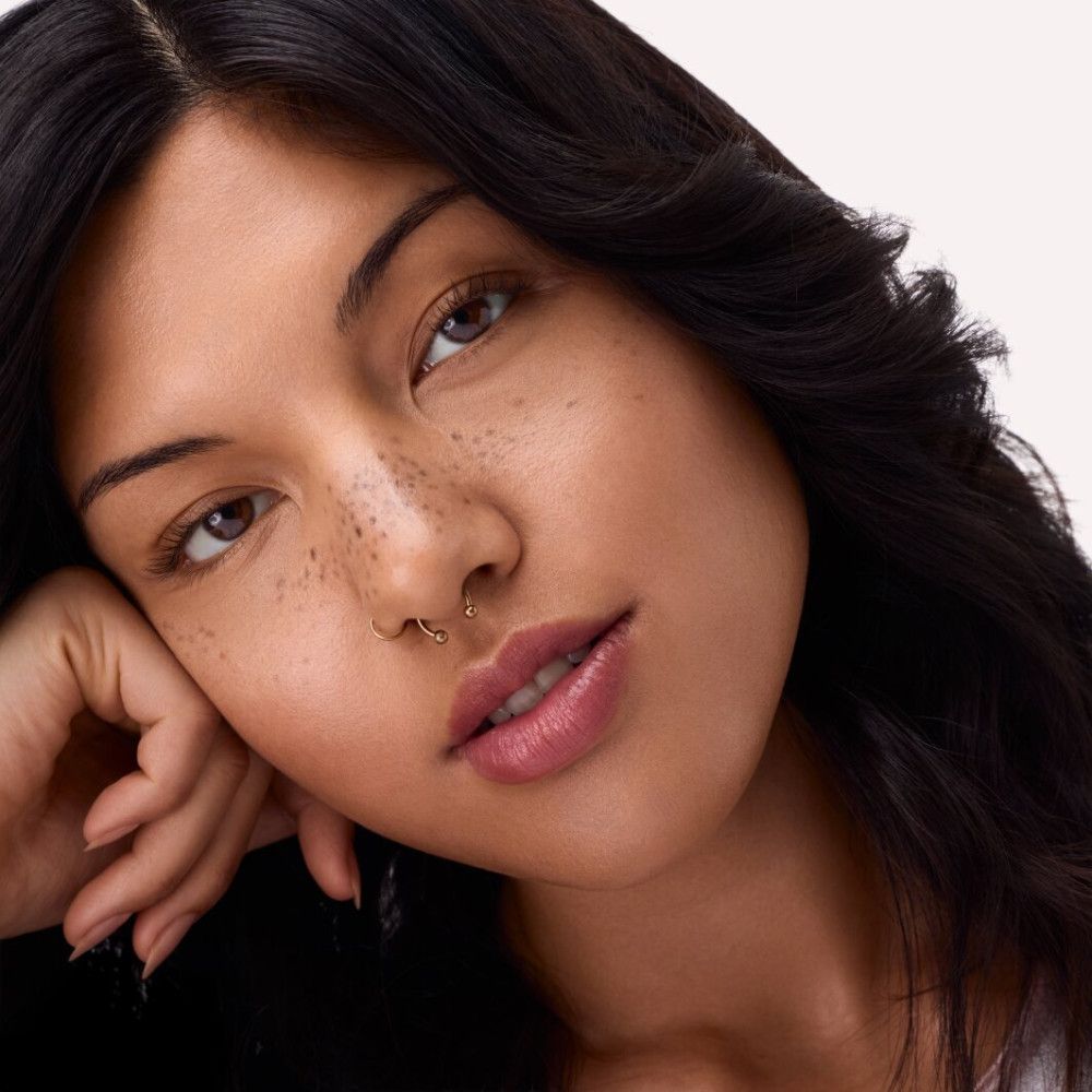 Porträt einer Frau. Frau mit dunklen Haaren, Sommersprossen und Lippenstift. Sie stützt ihr Kinn auf ihre Hand.