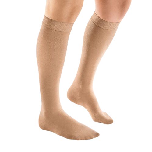 Hautfarbene Kompressionsstrümpfe am Bein einer Person. Die Strümpfe reichen bis zum Knie und haben einen feinen Abschluss.