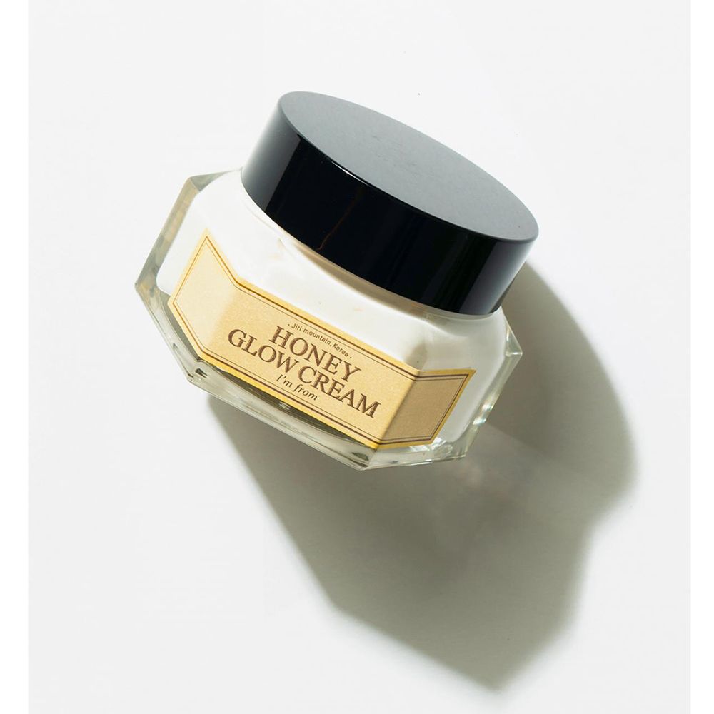 Creme-Glas mit schwarzem Deckel. Aufschrift: HONEY GLOW CREAM, I'm from. Gelbes Etikett. Schräge Ansicht.