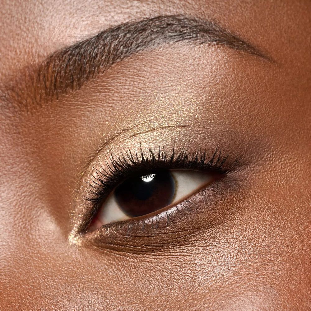 Nahaufnahme eines Auges mit goldfarbenem Lidschatten. Braune Augen, lange Wimpern, dunkle Augenbrauen. Hautton.