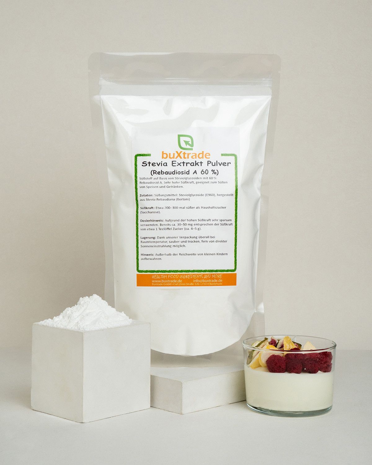 Buxtrade Stevia Extrakt Pulver in einem Standbodenbeutel, daneben ein Würfel mit Pulver und ein Glas mit Joghurt.