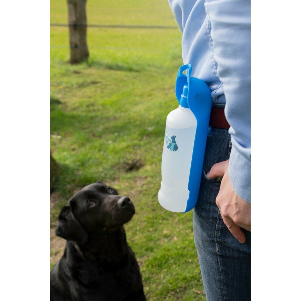 Person trägt blaue Trinkflasche am Gürtel. Schwarzer Hund schaut auf. Flasche hat blaue Halterung und weißen Behälter.
