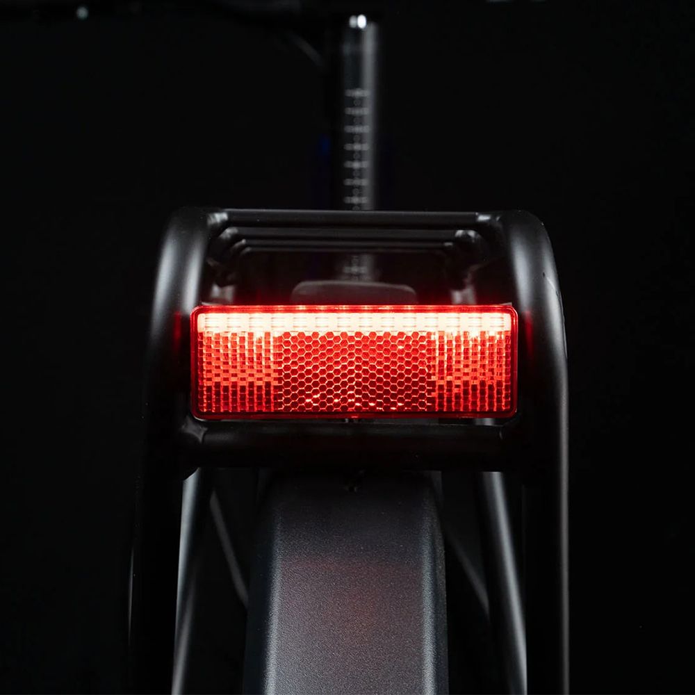 Rücklicht eines Fahrrads. Rotes, rechteckiges Licht. Schwarzer Rahmen. Schwarzer Hintergrund.