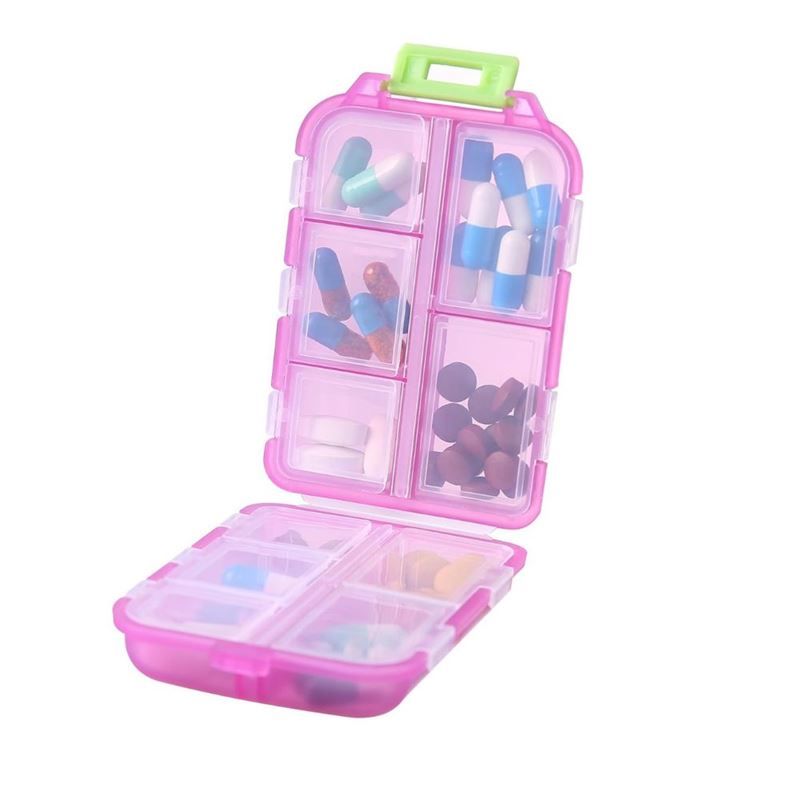 Pink Tablettenbox, offen, mit sieben Fächern. Jedes Fach enthält Pillen unterschiedlicher Farben und Formen. Grüner Griff.